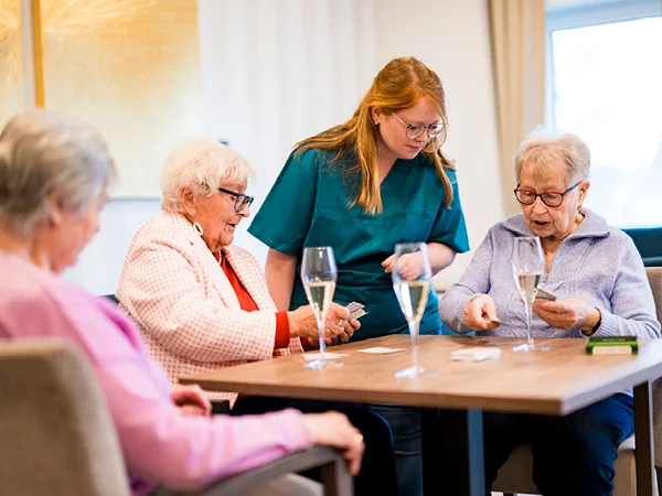 Pflegefachkraft mit Tagespflegeästen beim Kartenspielen
